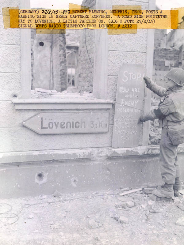MP Robert Fleming of the 407th Infantry Regiment, 102nd Infantry Division posting a warning sign in Kofferen, Germany in February 1945.