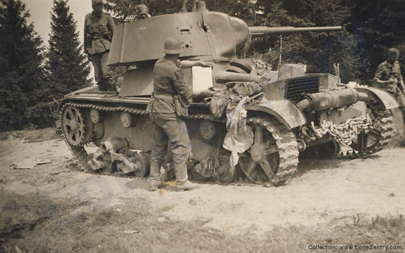 German troops inspect a destroyed Russian T-26 tank. The right-side of the conical turret has been penetrated just behind the vertical armor seam. The prominent engine vent with wire mesh screen can be clearly seen at the rear. No markings are visible.