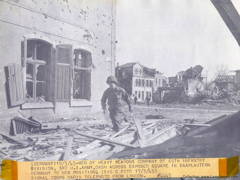 Signal Corps photo showing men of the 65th Infantry Division crossing the square in Saarlautern, Germany in March 1945.