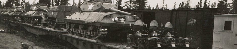 M10 tank destroyers, halftracks, and motorcycles are loaded on railcars in the United States. The boxcar in the background carries the emblem of the Chicago and North Western Line (CNW).