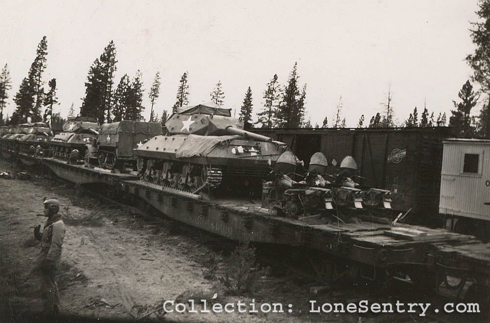 M10 tank destroyers, halftracks, and motorcycles are loaded on railcars in the United States. The boxcar in the background carries the emblem of the Chicago and North Western Line (CNW).