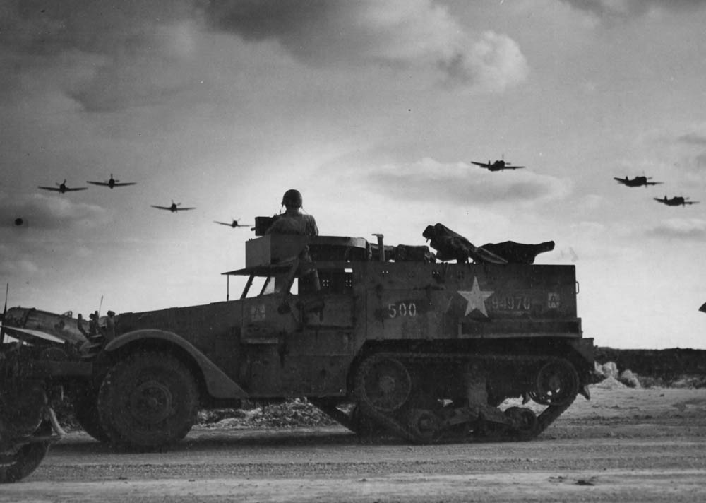 A halftrack on guard duty watches as a flight of Republic P-47 Thunderbolts of the 318th Fighter Group return to their airfield in the Okinawa Islands after a strike on Japan. (U.S. Air Force Photo)