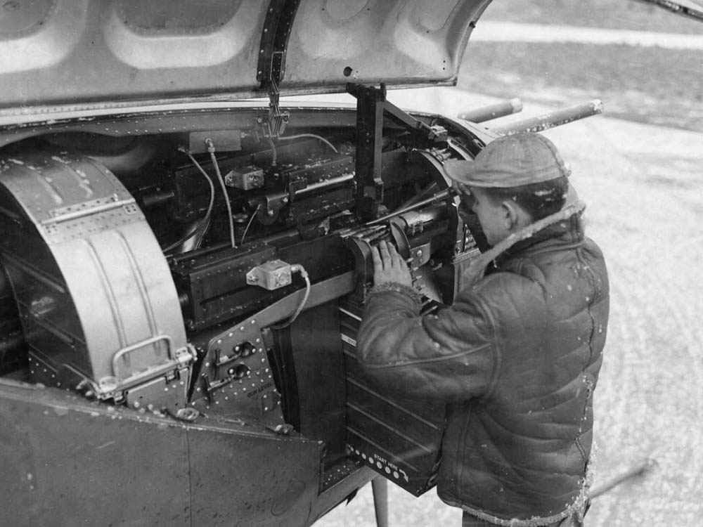 An armorer loads ammunition in the guns in the nose of a P-38 Lightning fighter. (U.S. Air Force Photograph.)