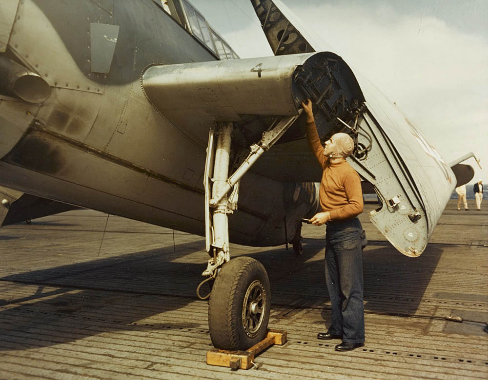 A plane caption inspects the landing gear of a Grumman TBF Avenger on the flight deck of a training escort carrier, circa 1943. (U.S. Navy Photo/National Archives.)