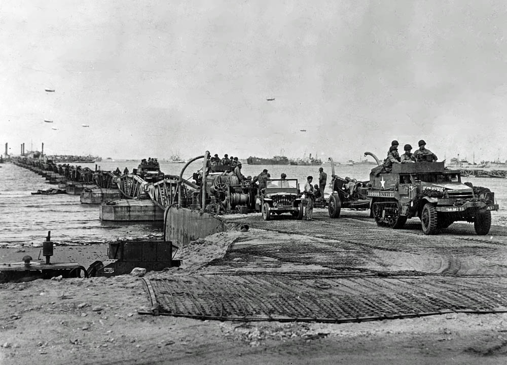 A jeep and a halftrack towing a howitzer lead a convoy of vehicles ashore on a floating causeways from a Mulberry harbor at Omaha Beach, June 1944.  (U.S. Army Signal Corps Collection, U.S. National Archives.)
