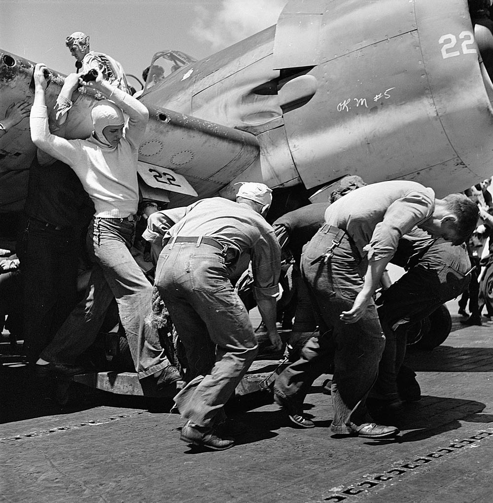 Sailors from the USS Lexington move an aircraft with a flat tire down the flight deck, November 1943. (U.S. National Archives Photograph.)