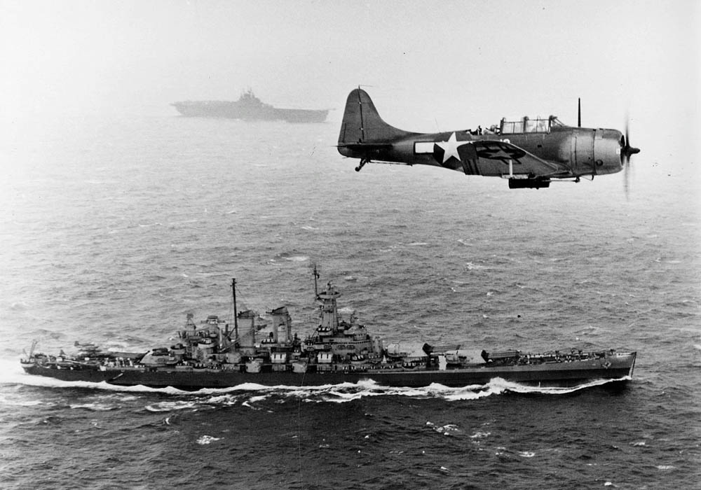 U.S. Navy Douglas SBD-5 Dauntless flies over the battleship USS Washington (BB-56) during the invasion of the Gilbert Islands, November 1943. (U.S. Navy Photograph.)