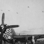 A group of Boeing B-17 Flying Fortress aircraft flies over a Republic P-47 Thunderbolt fighter on a field in England. (U.S. Air Force Photograph.)