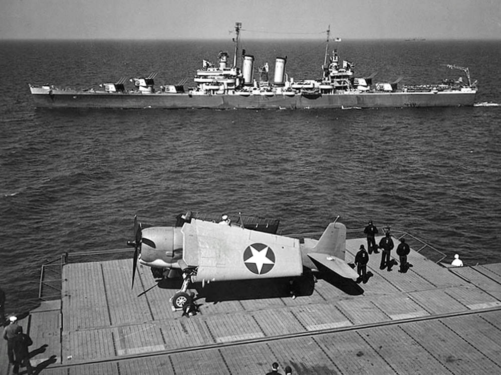 A Grumman F6F-3 Hellcat fighter is photographed on the aircraft carrier USS Yorktown as the U.S. Navy light cruiser USS Boise (CL-47) passes alongside. (U.S. Navy Photograph.)