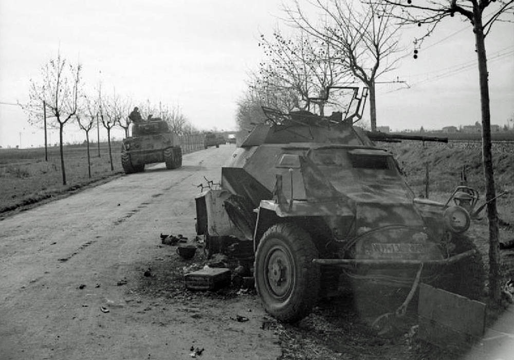 British Sherman tanks pass by a knocked-out German SdKfz 222 light armored car in Italy, January 1944.